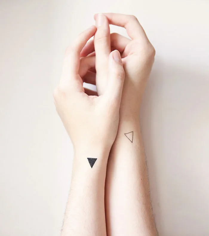 Minimalist tattoos on forearms featuring small triangle designs.