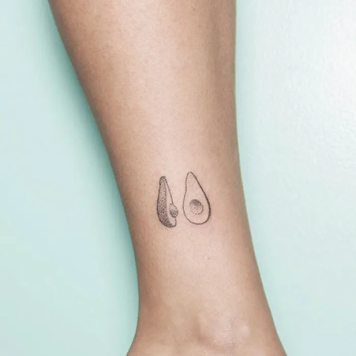 Minimalist tattoo of two avocado halves on an ankle.