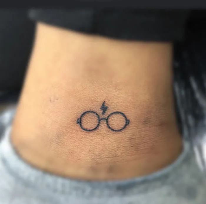 Minimalist tattoo of glasses with a lightning bolt on the neck.