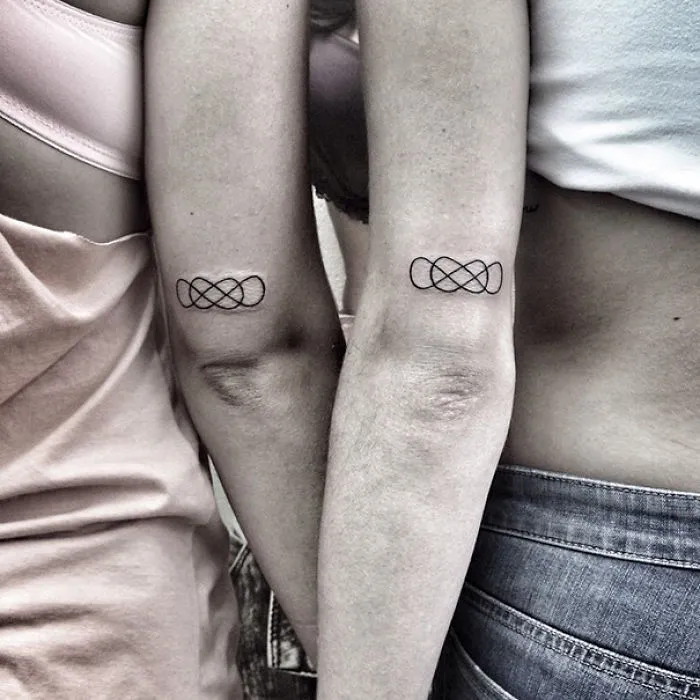 Minimalist tattoos on two arms, featuring a simple intertwined design in black ink.