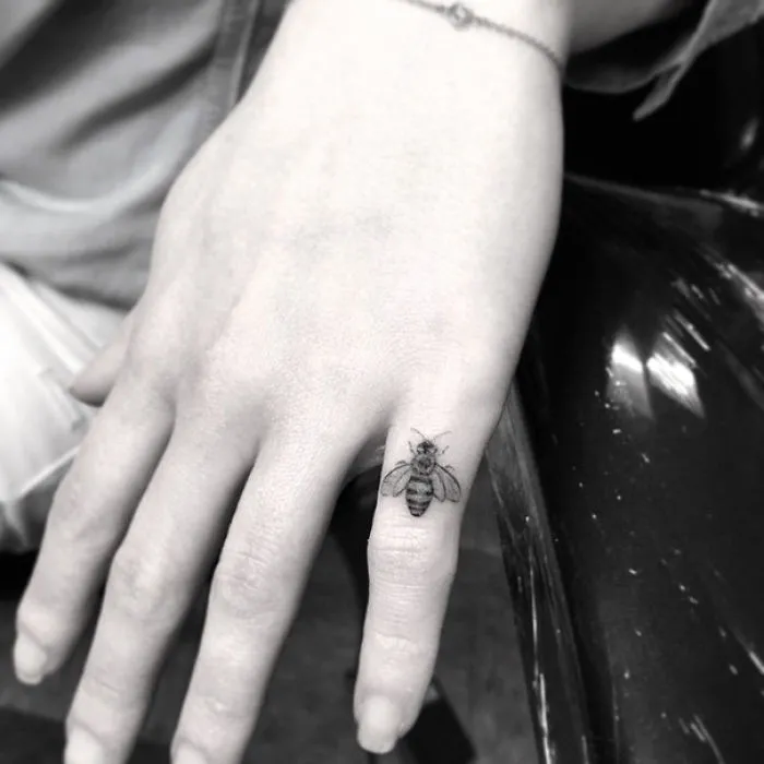 Minimalist bee tattoo on a finger, showcasing sleek ink design inspiration.