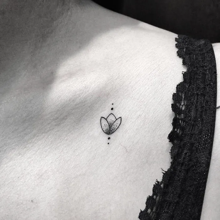 Minimalist tattoo of a small flower inked on the collarbone, adjacent to black lace fabric.