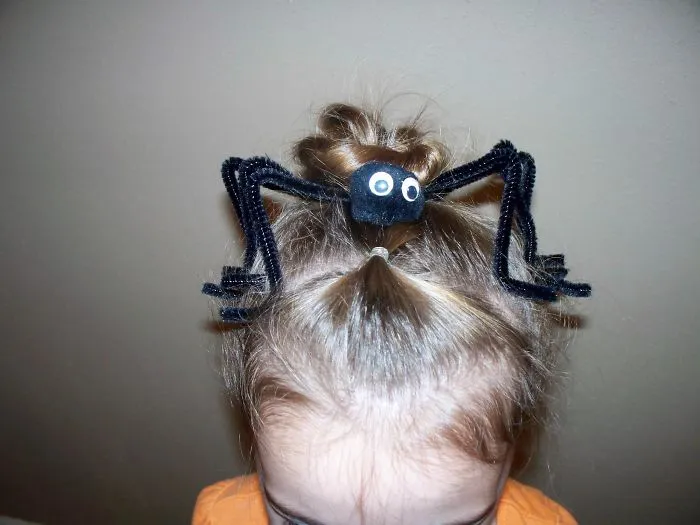 Child with a creative crazy hair day hairstyle, featuring a spider made of pipe cleaners on a bun.