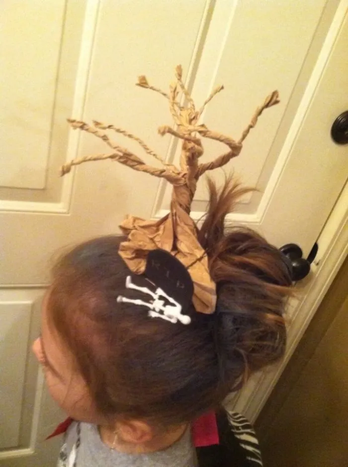 Creative crazy hair day style featuring a paper tree and "RIP" decoration on top of a bun.