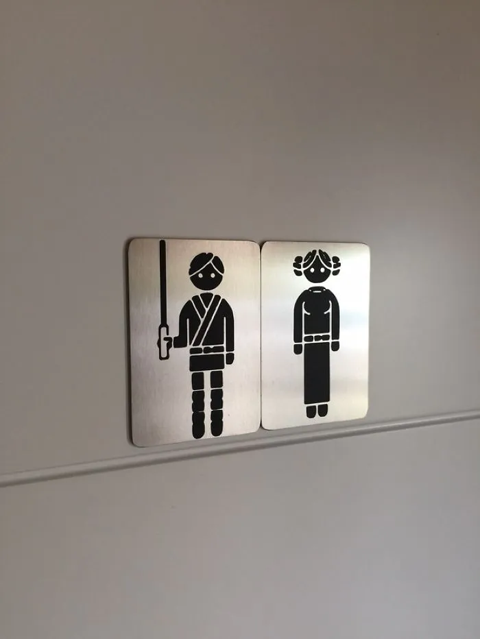 Funny bathroom signs with playful characters resembling sci-fi roles, adding humor to restroom entries.