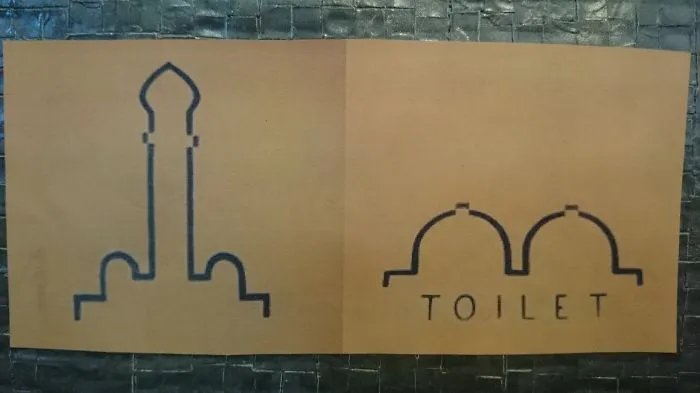 Funny bathroom signs featuring creative illustrations for toilets on a textured wall.