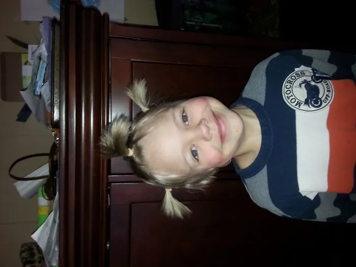 Child with crazy hair styled in spiky pigtails, smiling in a striped sweater.