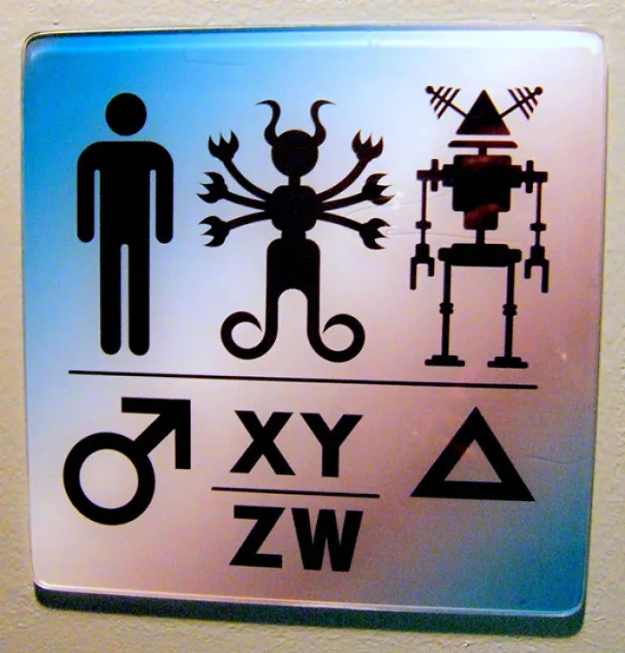 Funny bathroom sign with quirky symbols for male, alien, and robot figures.