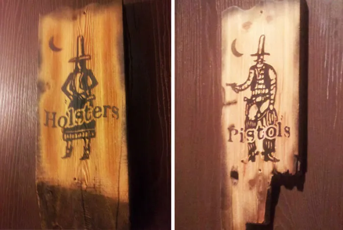 Funny bathroom signs on wooden boards labeled "Holsters" and "Pistols," featuring cowboy illustrations.