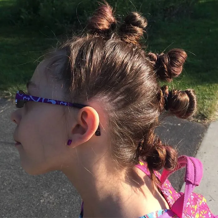 Child with creative hairstyle featuring multiple twisted buns for Crazy Hair Day, wearing purple glasses.