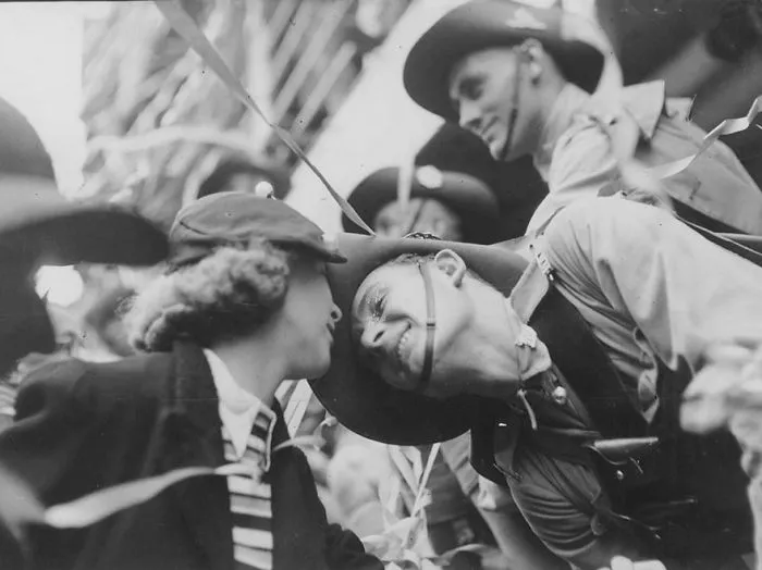 Couple embracing during wartime, surrounded by confetti and soldiers, capturing love amid historic events.