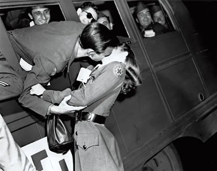 Historic photo of a soldier kissing a Red Cross nurse goodbye through a train window during wartime.