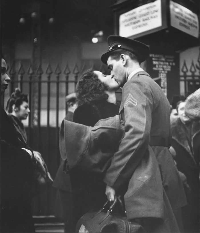 Historic wartime love captured as a soldier kisses a woman at a train station, holding his belongings tightly.