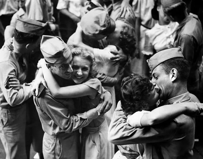 Soldiers in uniform embrace and kiss their loved ones during wartime in a historic black-and-white photo.