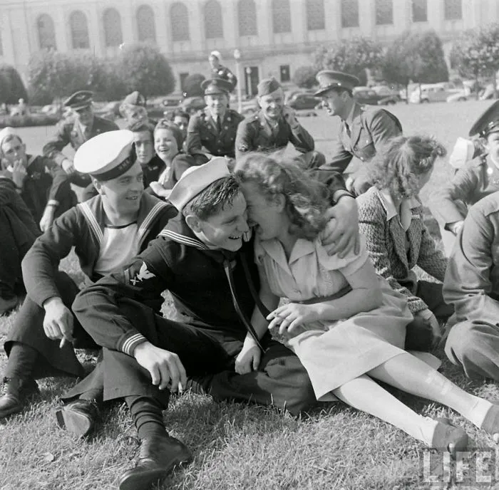 Sailor and woman embracing on a lawn, surrounded by soldiers during wartime; a historic photo of love in war.