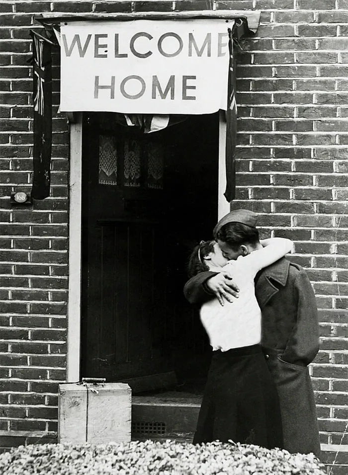 Historic wartime love photo: couple embracing under "Welcome Home" sign, capturing the emotional reunion.