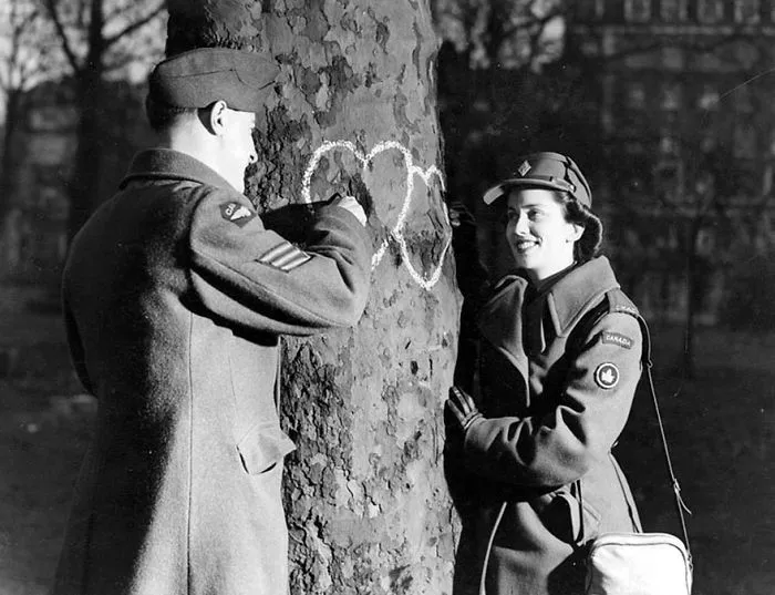 Soldier and woman during wartime standing by tree with chalk hearts, signifying love amidst conflict.