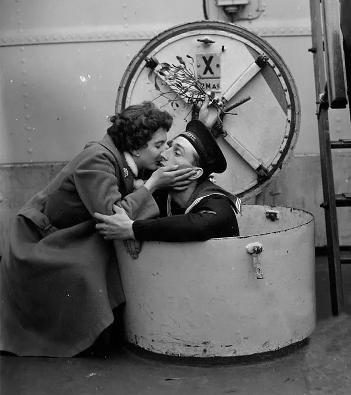 Sailor and woman sharing a kiss, showcasing wartime love with a submarine hatch in the background.