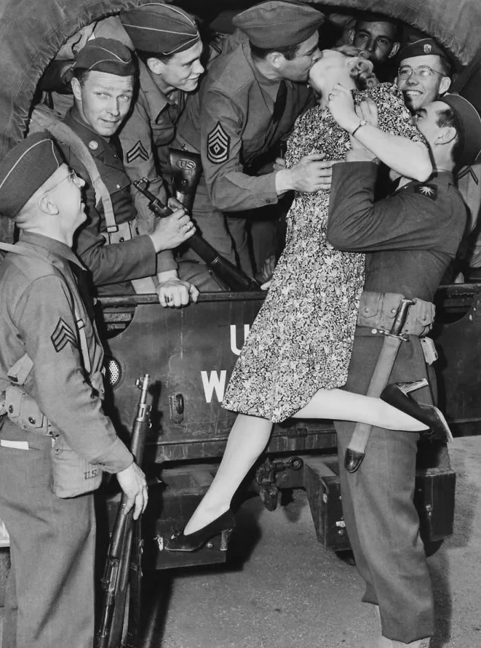 Soldier kissing a woman goodbye, surrounded by fellow soldiers, capturing love during wartime.