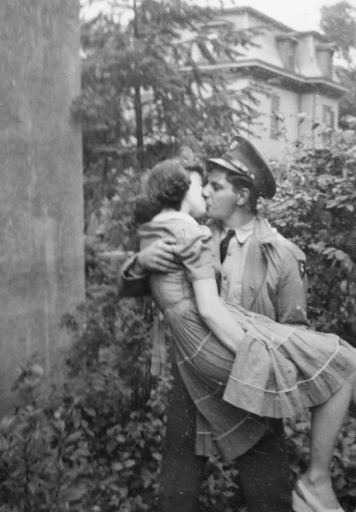 A soldier passionately kissing his partner during wartime, surrounded by greenery, capturing historic love moments.