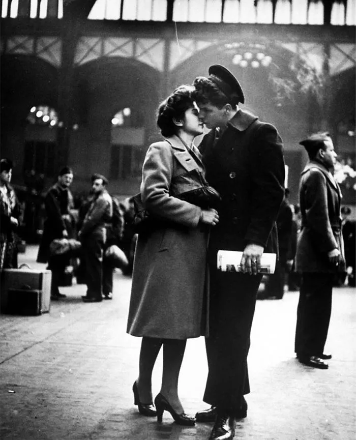 Couple kissing in a train station, capturing a moment of love during wartime.
