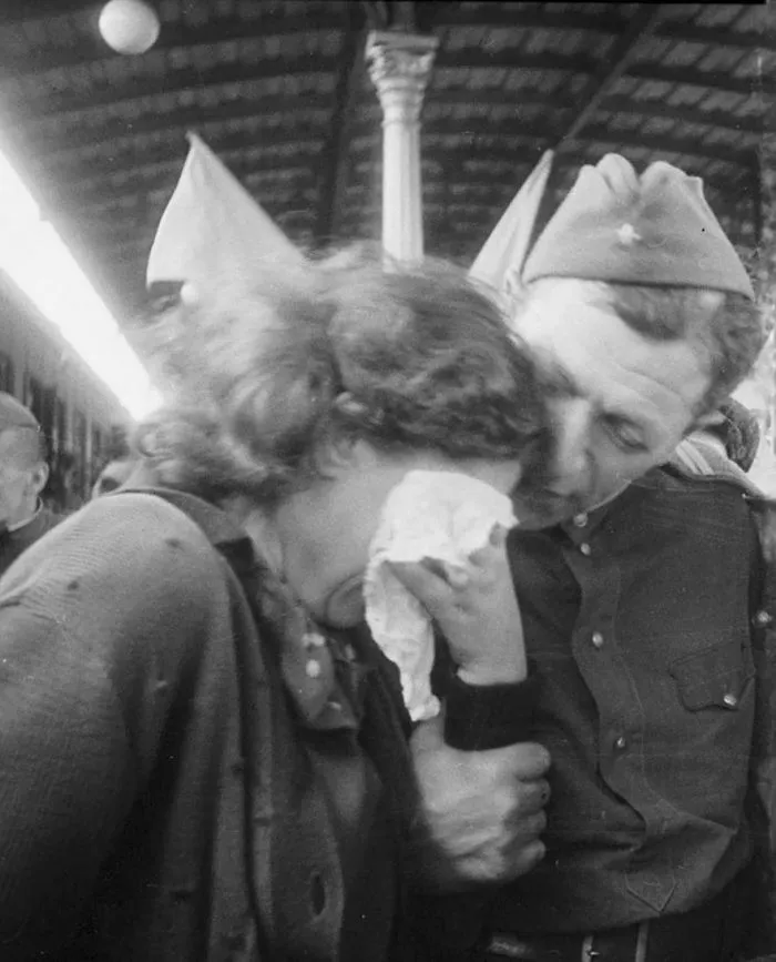Wartime couple embracing emotionally at a train station, capturing a moment of love and farewell.