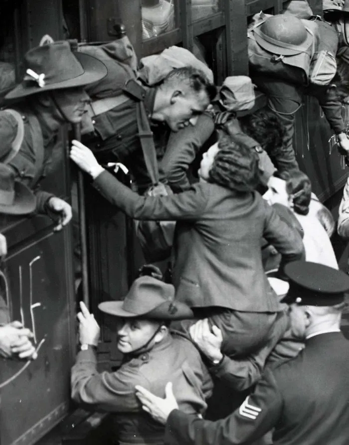 Soldiers and women embrace during wartime farewell at a train station.
