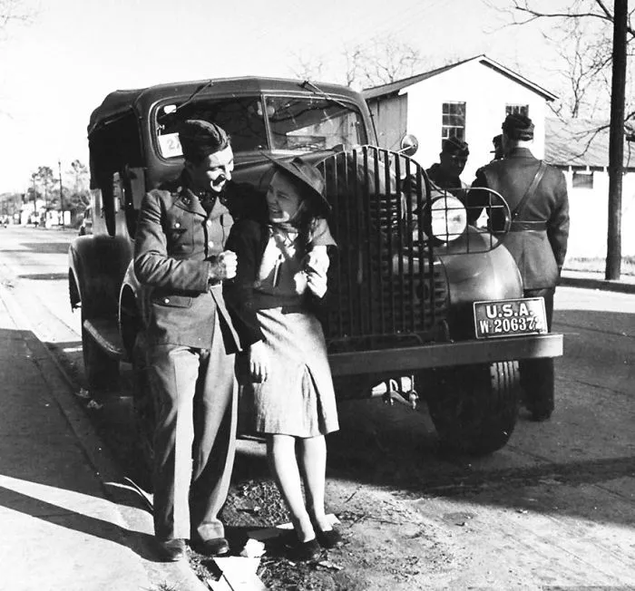Soldier and woman smiling in front of a military vehicle during wartime.