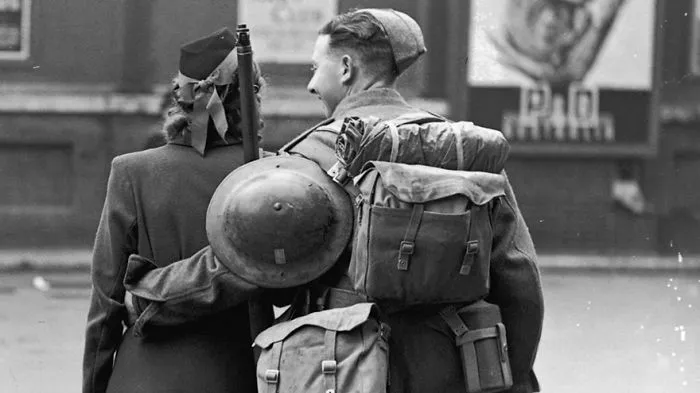 Soldier and woman walk arm-in-arm, showing love during wartime with military gear visible.