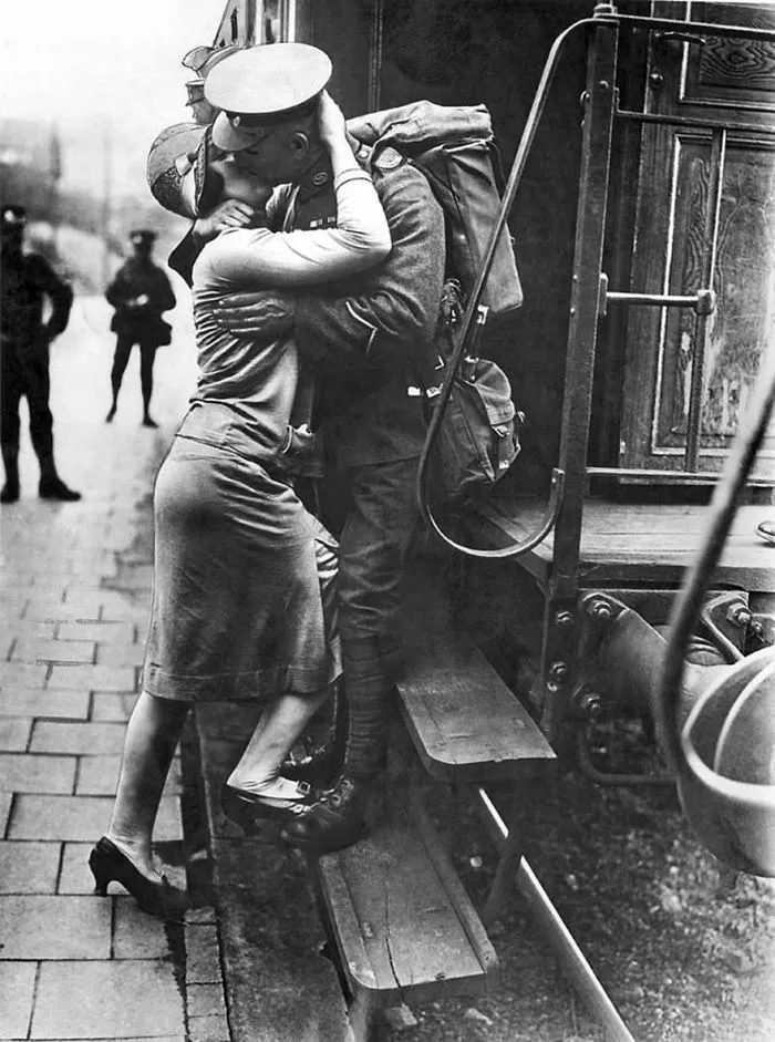 A soldier and a woman share an emotional kiss on a train platform, illustrating love during wartime.