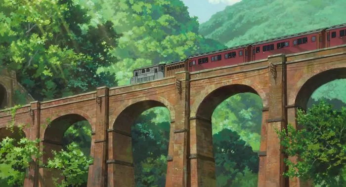 Studio Ghibli train crossing a brick bridge surrounded by lush greenery.