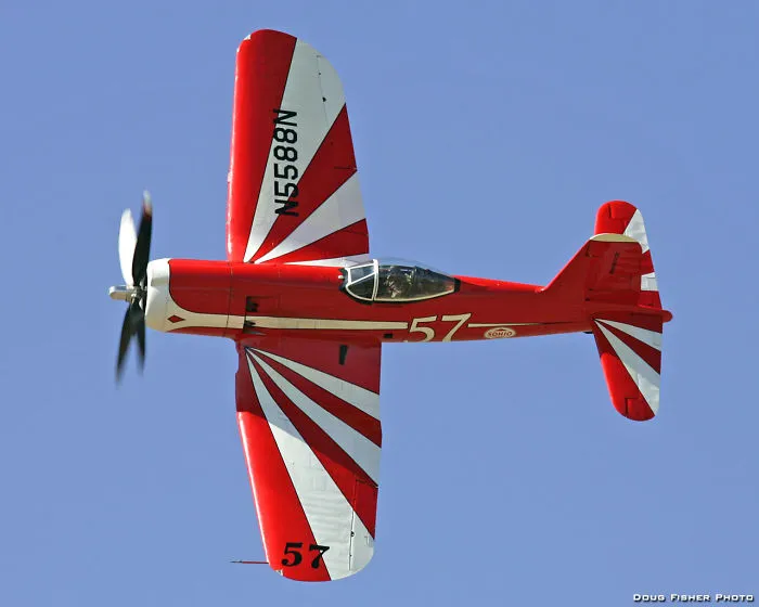 Red and white aircraft with propeller, flying against a clear sky, showcasing dynamic aerial design.