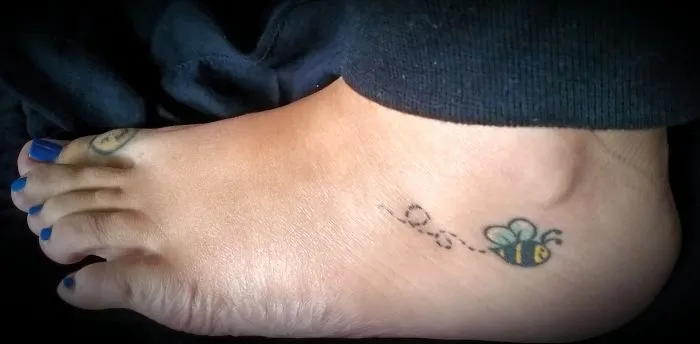 Small foot tattoo of a bee with a dotted flight path, showcasing a minimalist design.