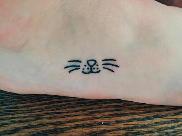 Minimalist small foot tattoo of a cat face, showcasing that less is more in tattoo design.