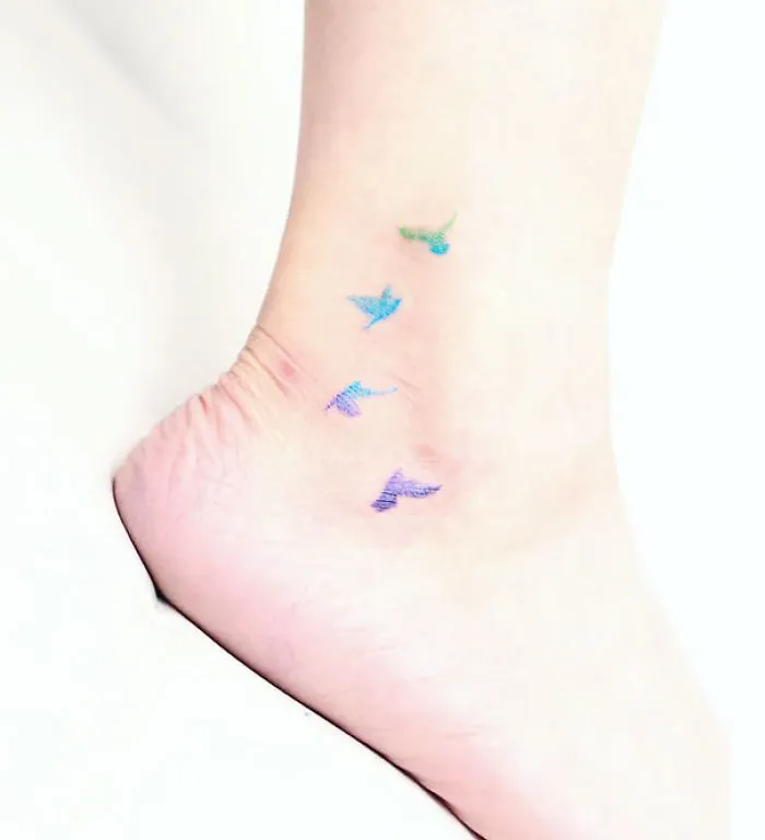 Colorful small foot tattoo featuring four birds in flight on the ankle.