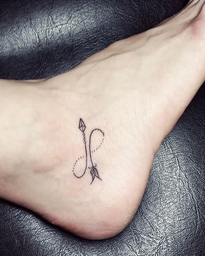 Small foot tattoo with delicate arrow and loop design on the side of the foot, showcasing minimalist ink art.