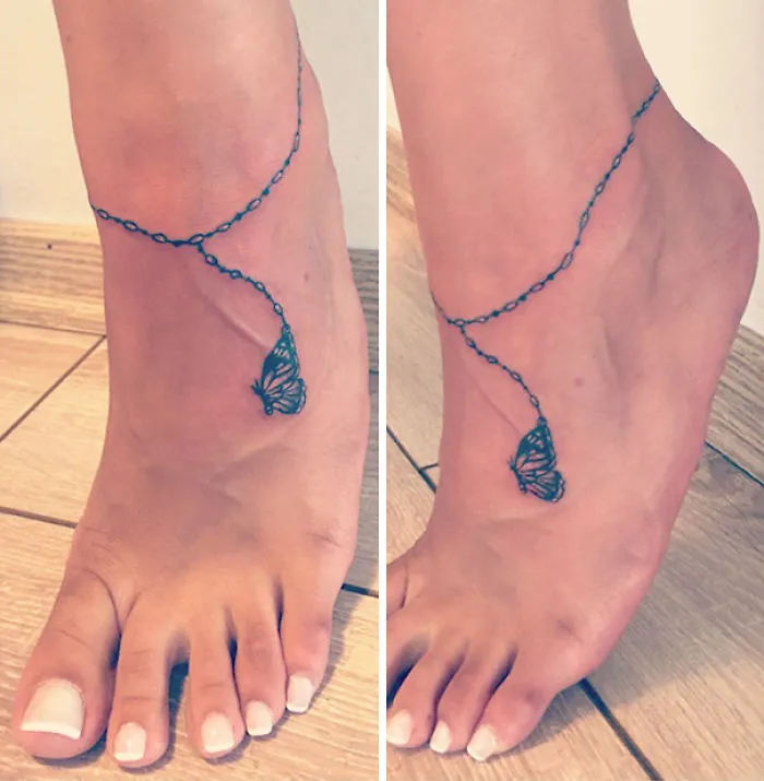 Minimalist small foot tattoo of a butterfly with ankle chain design, emphasizing less is more in tattoo art.