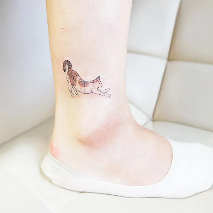 Small foot tattoo of a stretching cat in a minimalist style.