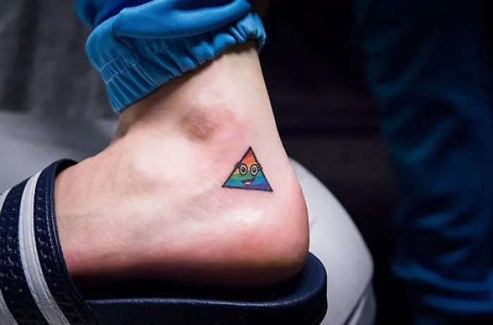 Small foot tattoo of a colorful triangle design on an ankle, showcasing minimalist art in a casual setting.