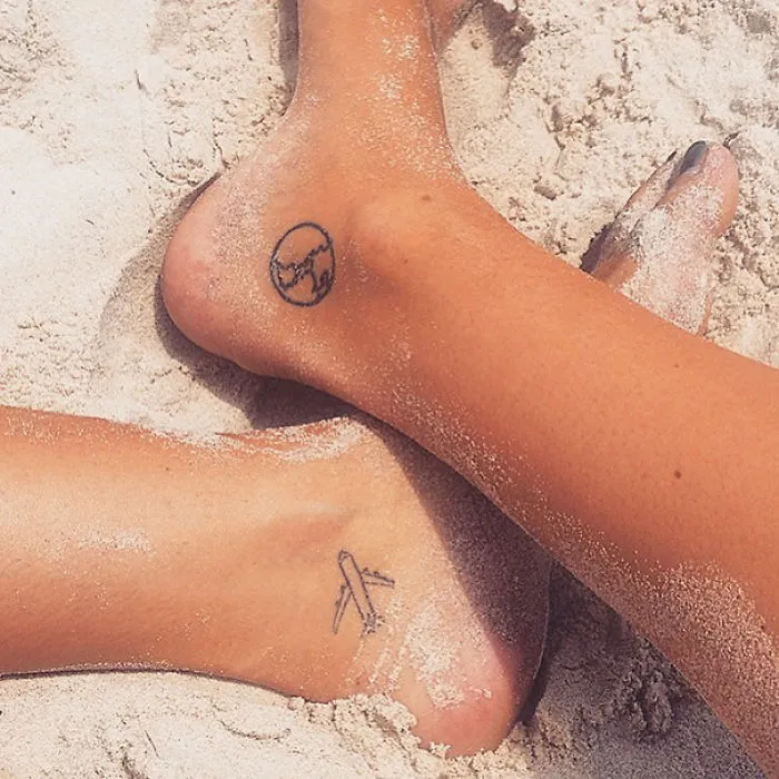 Small foot tattoo ideas featuring a world map and airplane designs on sandy feet.