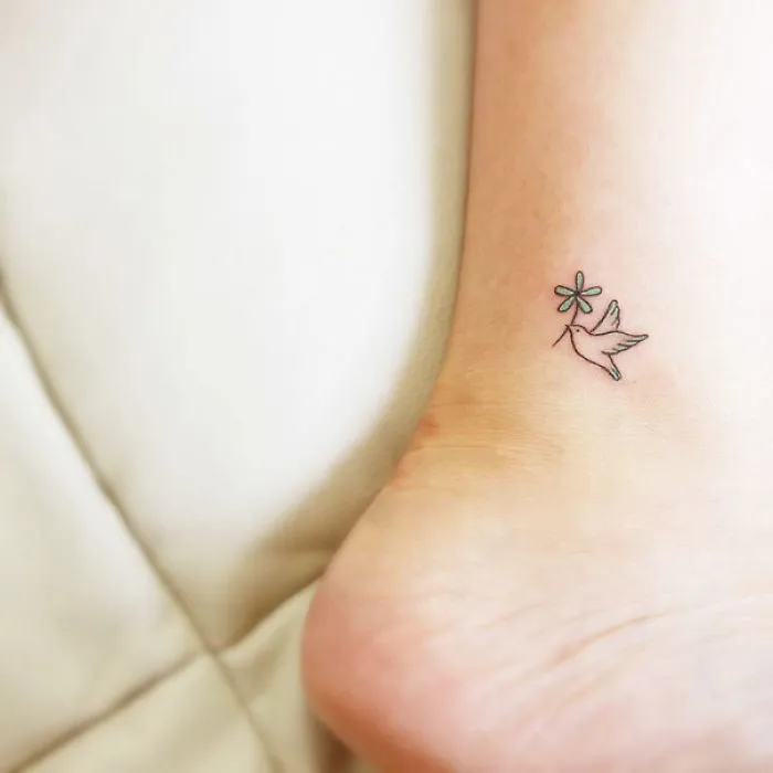 Minimalistic small foot tattoo of a bird with a flower.