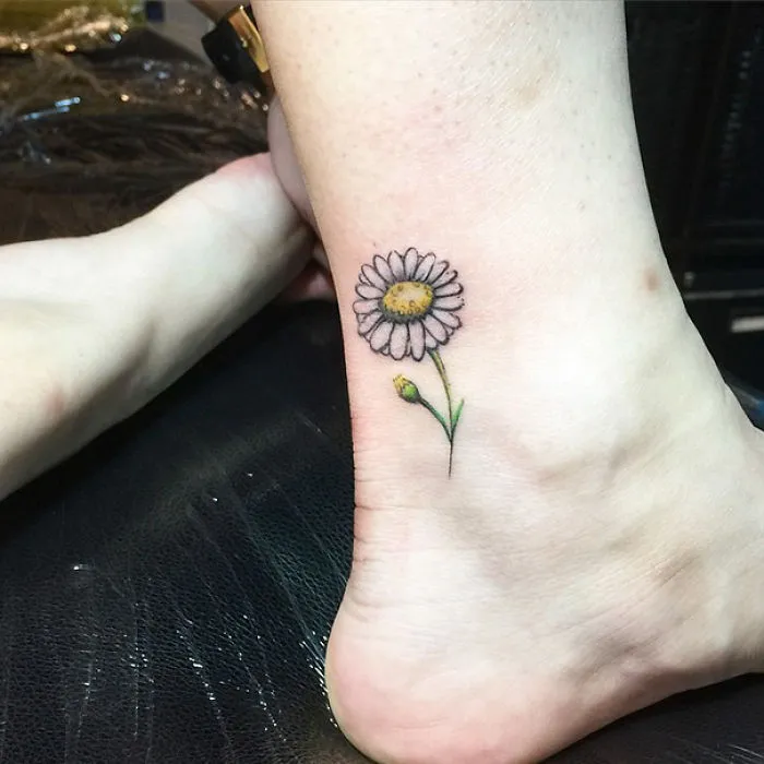 Small foot tattoo of a daisy on ankle, showcasing minimalist design.