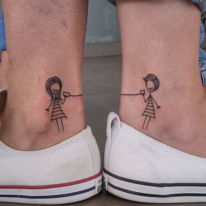 Cute minimal stick figure tattoos on ankles, featuring two people connecting, showcasing small foot tattoo ideas.