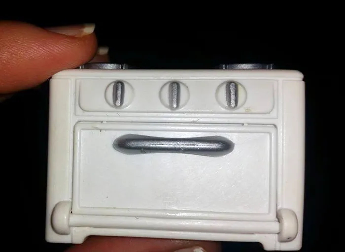 A regretted online purchase of a small, toy oven being held between fingers.