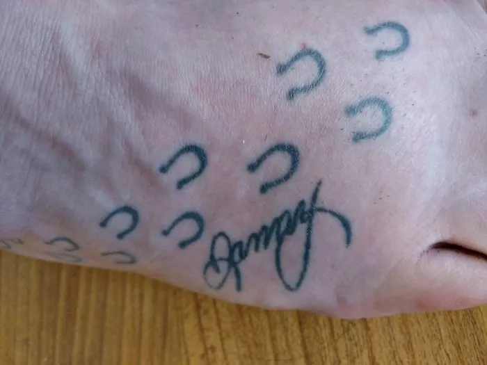Small foot tattoo with symbols and cursive lettering on skin.