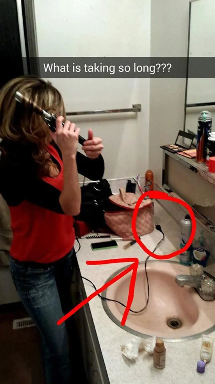 Woman styling hair with unplugged curling iron, humorous Snapchat moment.