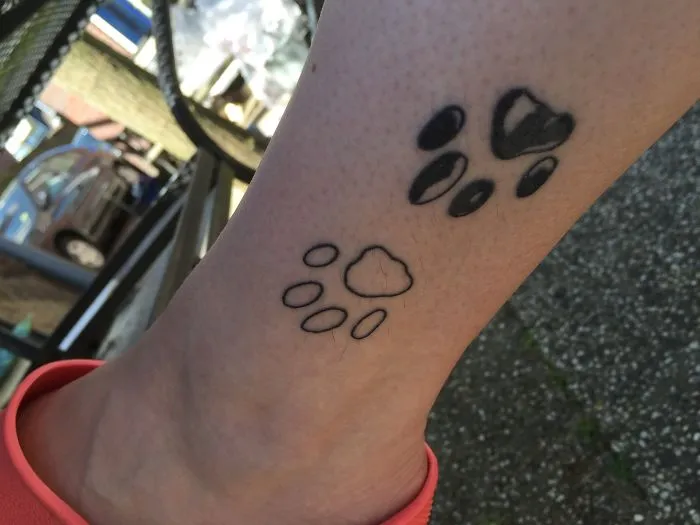 Paw print small foot tattoo with black ink and outline designs, showcasing minimalist art.