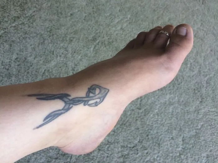 Small foot tattoo with a minimalist arrow design on a light carpet background.