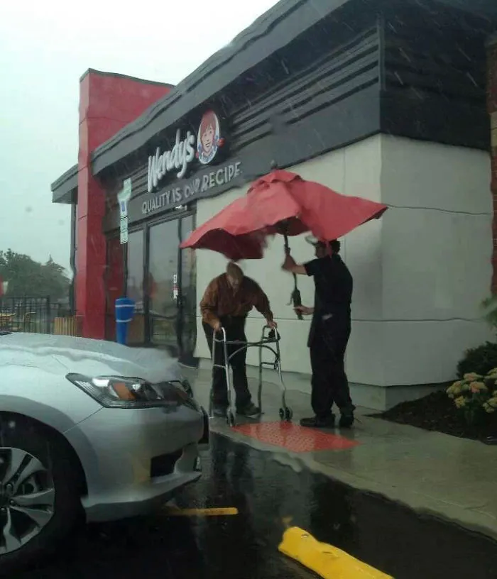 Wendy's Employee Removing Umbrella From A Table Outside To Walk Elderly Gentleman To His Car In The Rain