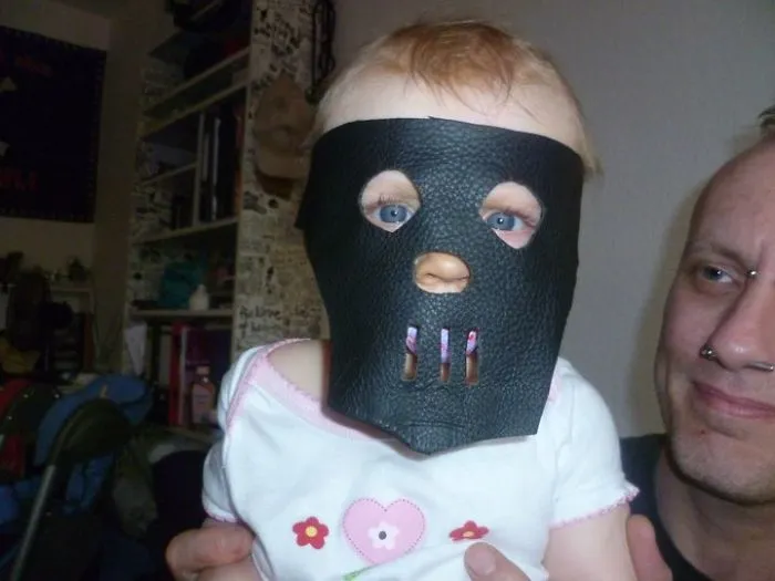 Baby wearing a leather mask being held by adult